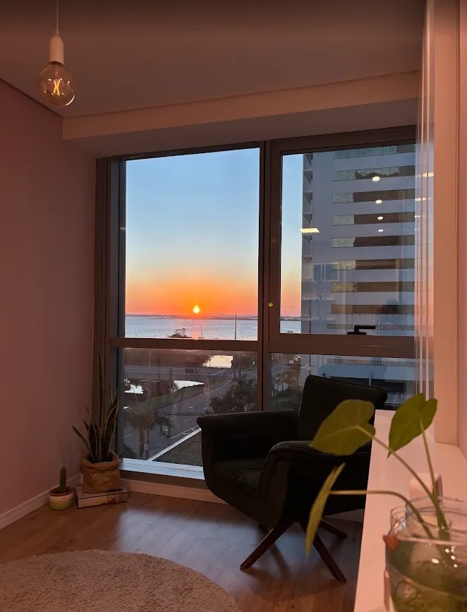Sala do consultório com poltrona e janela com vista para o Guaíba ao pôr do sol